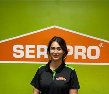 Brown haired female standing in front of a SERVPRO green background with a SERVPRO logo on the wall. 