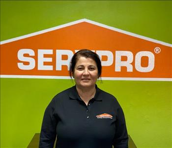 Brown haired female standing in front of a SERVPRO green background with a SERVPRO logo on the wall. 